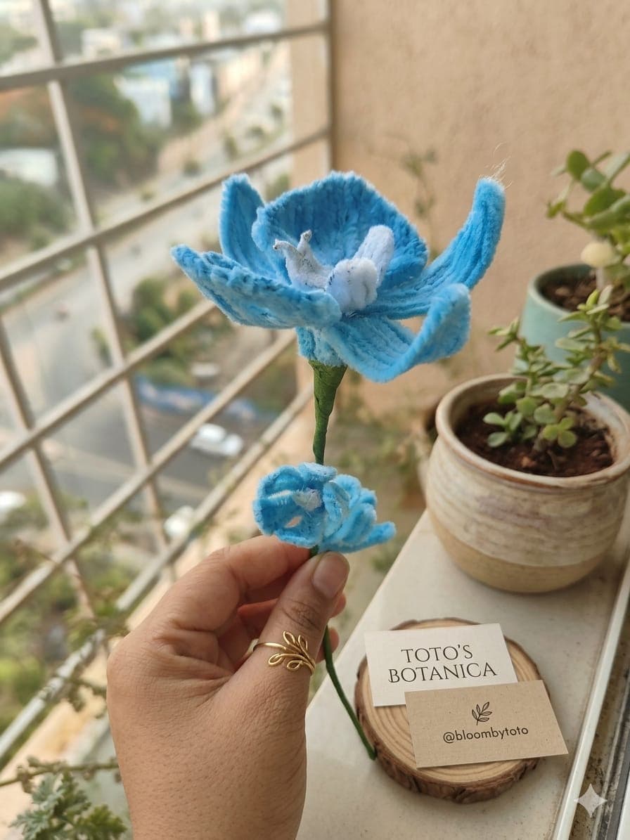 A crochet lotus with sky-blue petals around a soft white bloom.